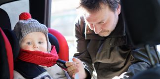 Father helps his son to fasten belt on car seat