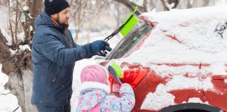 Father and daughter removing snow from car windows