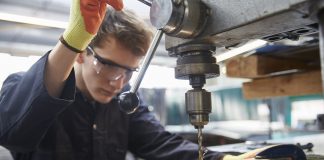 Young apprentice using pillar drill in steel fabrication factory